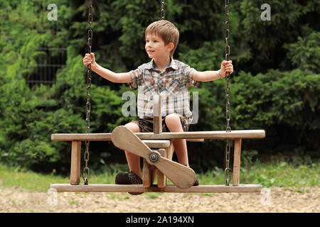 Fünf Jahre alten Jungen fliegen auf einer hölzernen Ebene schwingen im Sommer Park Stockfoto