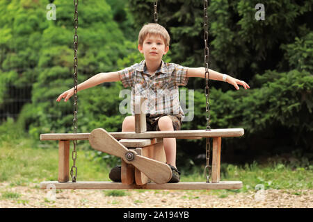 Fünf Jahre alten Jungen fliegen auf einer hölzernen Ebene schwingen im Sommer Park Stockfoto