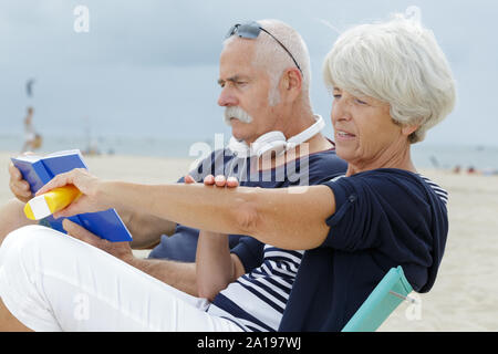 Ältere Paare am Strand Frau Anwendung Sonnencreme Stockfoto