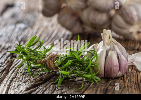 Knoblauchzehen und Zwiebel mit frischem Rosmarin auf alten Holztisch Stockfoto