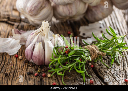 Knoblauchzehen Zwiebel mit frischem Rosmarin und Gewürzen auf alten Holztisch Stockfoto