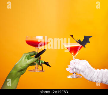 Foto der Hände von Mama und Zombies mit Wein Glas und schwarzem bat auf leere orange Hintergrund im Studio Stockfoto