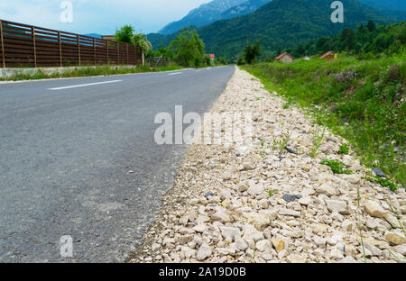 Asphaltierte Straße mit Kies auf der Seite führen zu den Bergen im Hintergrund Stockfoto