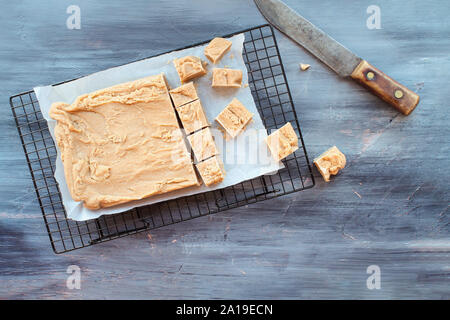 Block der köstlichen, hausgemachten Erdnussbutter Fudge in Quadrate über eine strukturierte Holz Tisch Hintergrund mit alten Messer schneiden. Bild geschossen von oben. Stockfoto