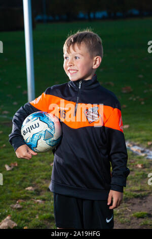 Ein acht Jahre alter Junge tragen ein Fußball-Streifen und halten ein Fußball unter dem Arm. Stockfoto