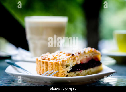 Dreieckige Stück Mohn Torte und eine Gabel mit Puderzucker auf dem Hintergrund einer transparenten Glas mit weißem Kaffee und eine gelbe Schale Stockfoto