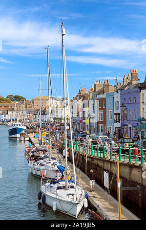 Yachten auf dem Kai in der Alte Hafen mit bunten Geschäften, Restaurants und Eigenschaften in Trinity Road, Weymouth, Jurassic Coast, Dorset, England, Großbritannien Stockfoto