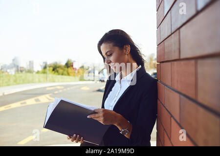 Seriöse Geschäftsfrau ist Lesen von Dokumenten beim Stehen im Freien. Stockfoto