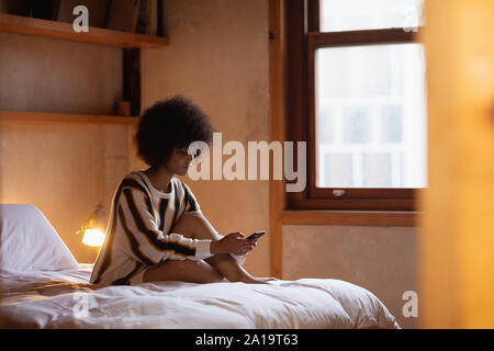 Junge Frau mit Smartphone im Bett Stockfoto