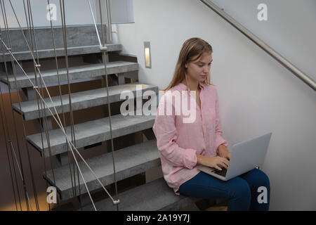 Blonde junge Frau sitzt auf der Treppe mit Laptop Stockfoto