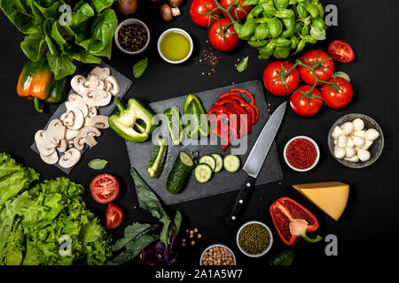 Rohzutaten zum Kochen vegetarisch gesunde Lebensmittel. Flache Lay von Gemüse und Käse auf schwarzem Hintergrund. Stockfoto