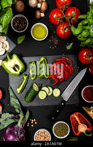 Rohzutaten zum Kochen vegetarisch gesunde Lebensmittel. Flache Lay von Gemüse und Käse auf schwarzem Hintergrund. Stockfoto