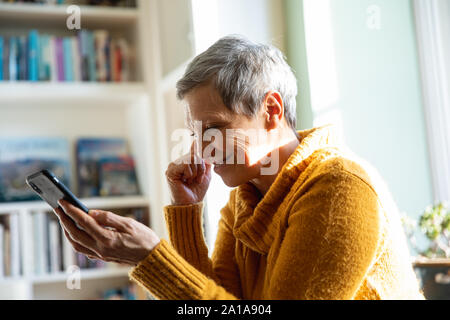 Reife Frau alleine zu Hause mit Smartphone Stockfoto