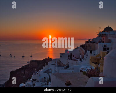 Majestätischen Blick auf orange Sonne über ruhigen Wasser mit Boote und die Altstadt von Oia auf Santorini in Griechenland Stockfoto