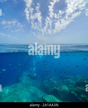 Seascape des Mittelmeers, viele Fische mit Taucher unter Wasser und blauer Himmel mit Wolken, geteilte Ansicht über und unter Wasser Oberfläche, Frankreich Stockfoto