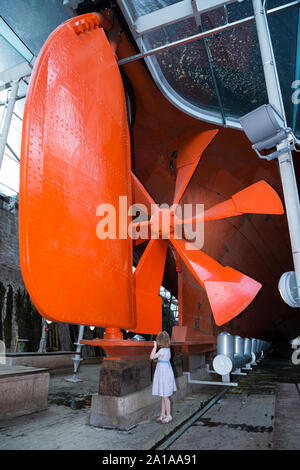 Kind Gast touristische Kinder geben zu Schraube Isambard Kingdom Brunel's Propeller, Ruder- und Schiffskörper der SS Great Britain, unter der gläsernen Meer im Trockendock, Dockyard Museum in Bristol. Großbritannien (109) Stockfoto