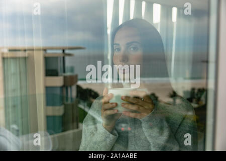 Junge Frau mit einer Tasse Kaffee aus Fenster Stockfoto