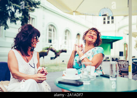 Zwei glückliche älterer Frauen reden, Kaffee trinken, während Sie einander sitzen, die in der Tabelle in einem Café im Freien. Stockfoto