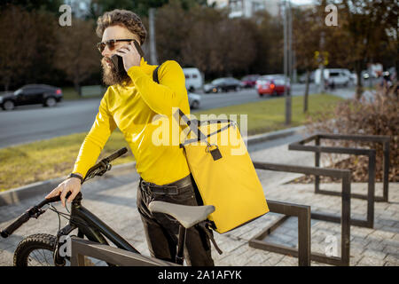 Junge Bartgeier Kurier Lieferung von Nahrung in thermischen Tasche auf dem Fahrrad, im Gespräch mit einem Kunden auf die Stadt. Stockfoto