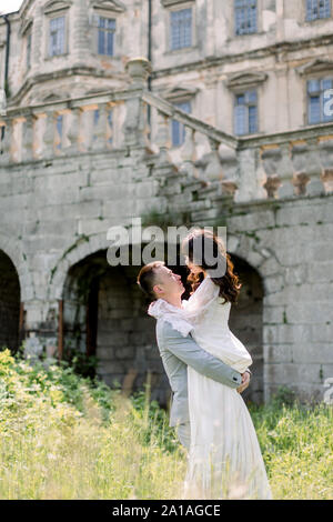 Wunderschöne wunderschöne chinesische Braut und Bräutigam walking im sonnigen Tag und Küssen. happy Hochzeit paar umarmen, Mann Frau hält, im Freien in der Nähe der alten Burg Stockfoto