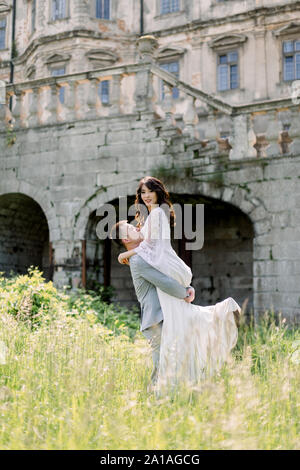 Wunderschöne wunderschöne chinesische Braut und Bräutigam walking im sonnigen Tag und Küssen. happy Hochzeit paar umarmen, Mann Frau hält, im Freien in der Nähe der alten Burg Stockfoto