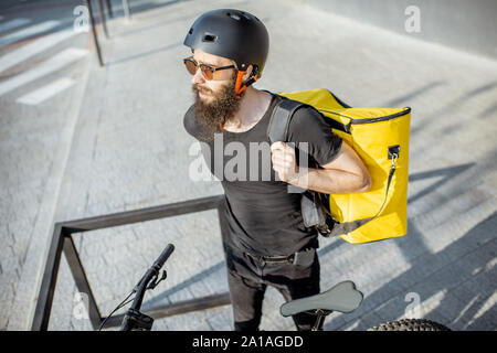 Männliche Kurier tragen thermische Rucksack für Essen Lieferung auf einem Fahrrad Parkplatz im Freien. Essen Konzept Stockfoto