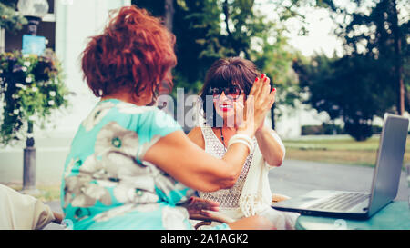 Gerne ältere weibliche Freunde geben High Five, Erfolg feiern, während Sie einander sitzen, die in der Tabelle in einem Café im Freien. Stockfoto