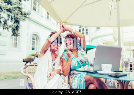 Gerne ältere weibliche Freunde geben High Five, Erfolg feiern, während in der Tabelle in einem Café im Freien sitzen. Stockfoto