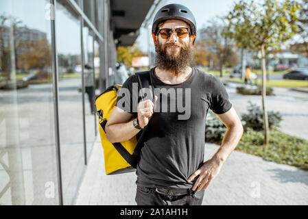 Portrait einer jungen Bartgeier Kurier in Schutzhelm mit gelben thermal Bag für Essen, die auf der Straße im Freien Stockfoto