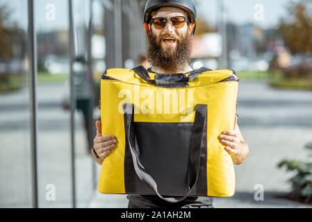 Portrait einer jungen Bartgeier Kurier stehend mit gelben thermal Bag für Essen, die auf der Straße im Freien Stockfoto