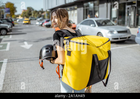 Portrait einer jungen und freundlichen weiblichen Kurier stehend mit gelben thermische Rucksack, Bereitstellung von frischen Produkten im Freien Stockfoto