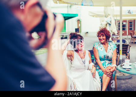 Der Fotograf macht ein Foto mit zwei Glückliche älterer Frauen in einem Café im Freien sitzen. Stockfoto