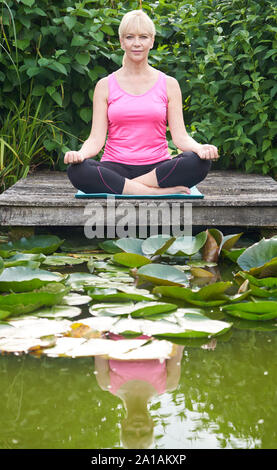 Portrait von reife Frau in Yoga Position auf hölzernen Steg am See Stockfoto