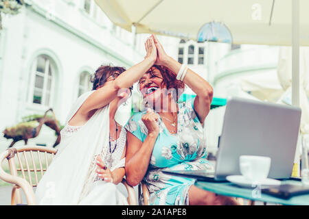 Gerne ältere weibliche Freunde geben High Five, Erfolg feiern, während Sie einander sitzen, die in der Tabelle in einem Café im Freien. Stockfoto