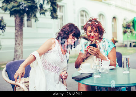 Zwei bekommt Frauen trinken Kaffee und mit Telefon im Cafe. Stockfoto