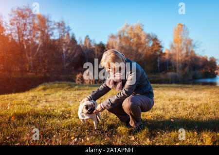 Wandern mops Hund im Herbst Park am Fluss. Glückliche Frau spielen mit Pet und Spaß mit bester Freund. Stockfoto