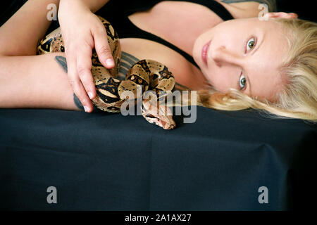 Portrait von Mädchen mit Boa constrictor Schlange. Schöne Frau hält Schlange in der Hand und vor der Kamera posieren. Exotischen tropischen kaltblütige Reptilien. Stockfoto