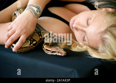 Portrait von Mädchen mit Boa constrictor Schlange. Schöne Frau hält Schlange in der Hand und vor der Kamera posieren. Exotischen tropischen kaltblütige Reptilien. Stockfoto
