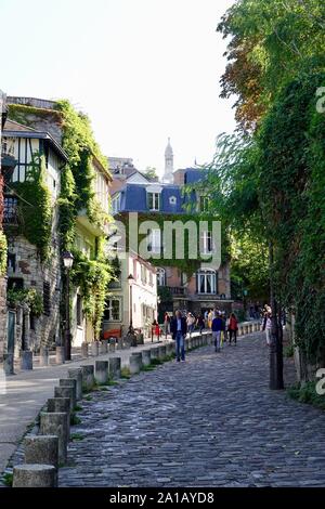 Menschen, die die gepflasterte Straße rue de L'Abreuvoir in der malerischen, dörflichen Nachbarschaft von Montmartre, Paris, Frankreich, hinunter gehen. Stockfoto
