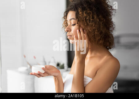 Schwarze Frau mit Gesicht Creme Jar stehend im Bad Stockfoto