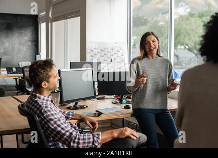 Junge Designer im Gespräch mit Kolleginnen und Kollegen während eines beiläufigen Büro Sitzung Stockfoto