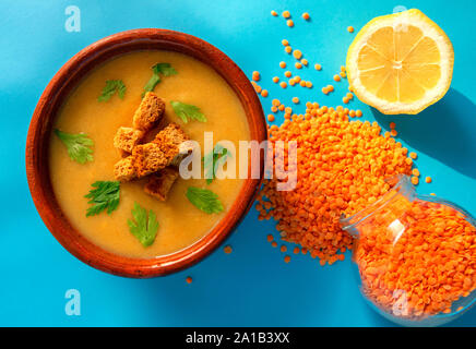 Frische Linsen creme Suppe in eine braune Schale auf blauem Hintergrund. Ansicht von oben. Linsen Grütze im Glas und frischer Zitrone. Linsensuppe Stockfoto