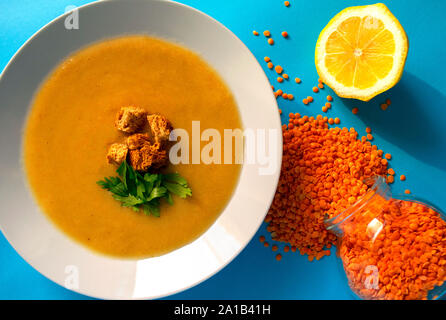 Frische Linsen creme Suppe in Weiß auf blauem Hintergrund. Ansicht von oben. Linsen Grütze im Glas und frischer Zitrone. Linsensuppe Stockfoto