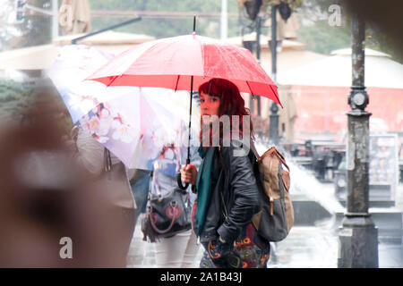 Belgrad, Serbien - September 24, 2018: Blurry junge Frau zu Fuß unter der rote Regenschirm an regnerischen und Masse Ort Straße Stockfoto