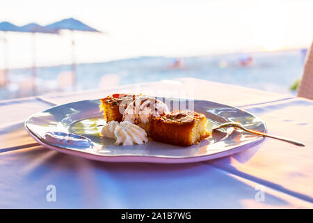 Zwei Stücke des Kreisdiagramms mit Eis in eine weiße Platte aufgehellt mit Sonnenuntergang Sonne, Meer und Strand Sonnenschirme auf dem Hintergrund Stockfoto