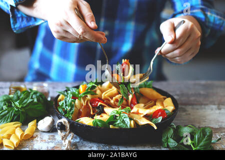 Koch mixe Nudeln mit Basilikum und Gewürzen in einen Topf. Leckere Nudeln in einer Pfanne mit Tomaten, Basilikum und Gewürzen. Ein Topf Nudeln. Italienische vegan Pasta. Wählen Sie Stockfoto