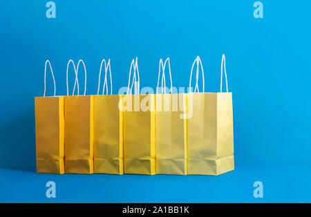 Papier Einkaufstüten in einer Reihe, in den Farben gelb, auf minimalistische blauen Hintergrund. Christmas shopping Thema. Gifting Konzept. Bunte präsentiert Taschen Stockfoto