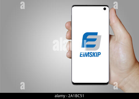 Ein Mann hält ein Smartphone mit dem Logo der Firma Eimskipafélag Íslands auf Nasdaq Island aufgeführt. Grauen Farbverlauf Hintergrund. Credit: PIXDUCE Stockfoto