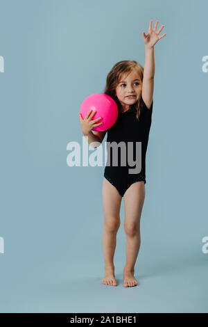 Kleines Mädchen in einem schwarzen Body mit rosa Gymnastikball über blauer Hintergrund Stockfoto