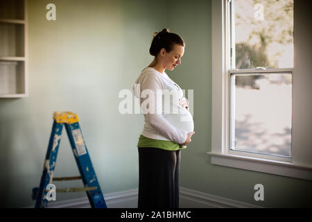 Seitenansicht einer schwangeren Frau stand neben einem Fenster. Stockfoto